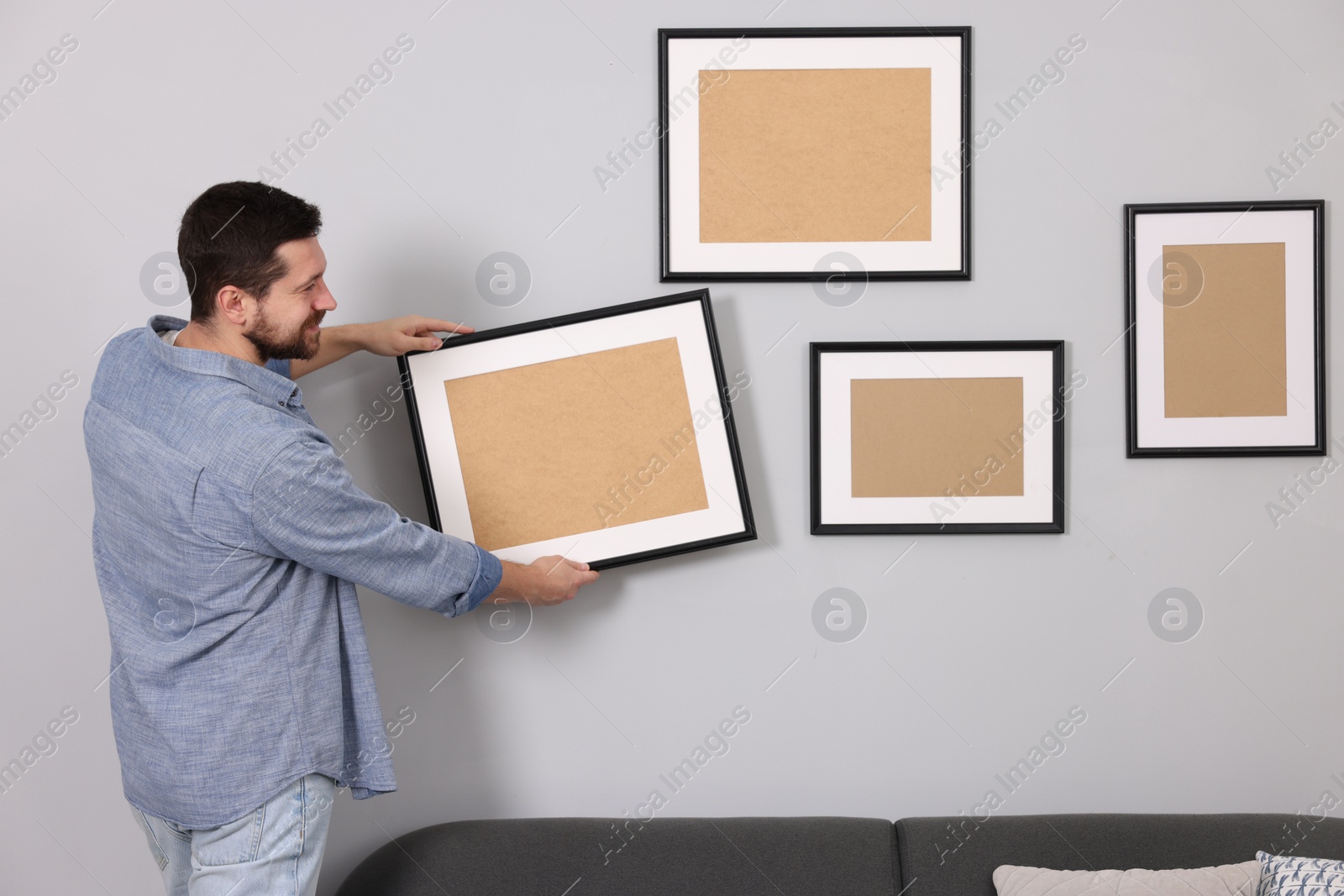 Photo of Man hanging picture frame on gray wall indoors