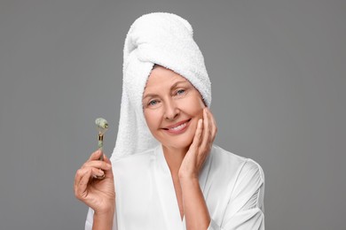 Woman with jade roller on grey background. Facial massage