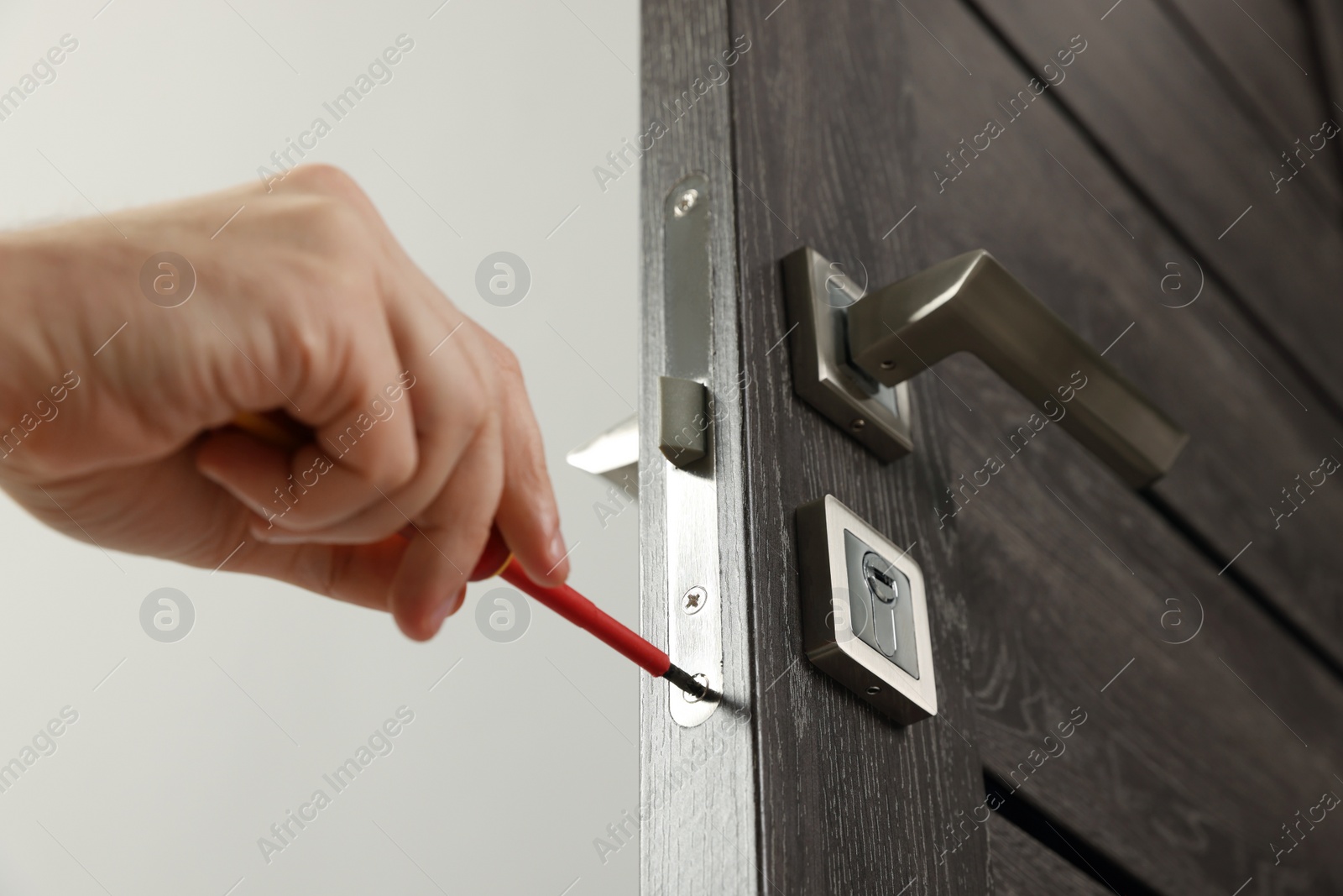 Photo of Worker with screwdriver repairing door lock indoors, closeup