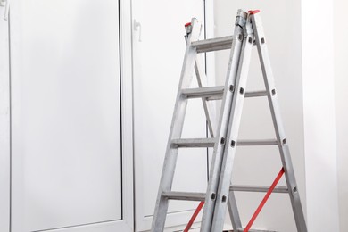 Metal folding ladder near closed window indoors. Space for text