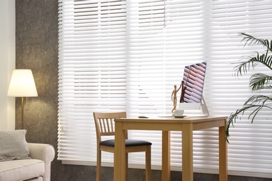 Photo of Comfortable workplace near window with blinds in room