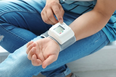 Photo of Young man checking pulse with blood pressure monitor on wrist, closeup