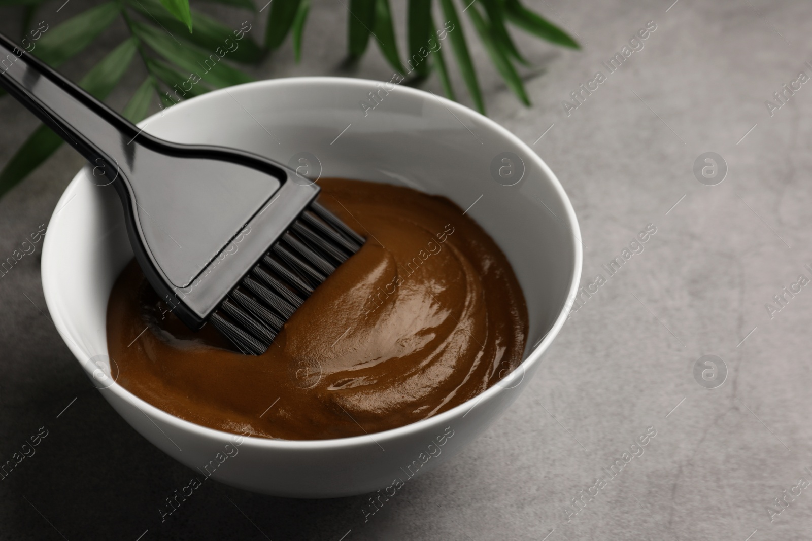 Photo of Bowl of henna cream and brush on light grey table, closeup with space for text. Natural hair coloring