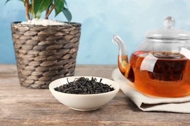 Photo of Bowl with dry tea and glass pot of hot beverage on table