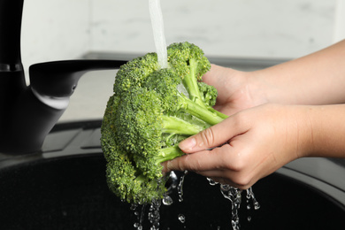 Photo of Woman washing fresh green broccoli in kitchen sink, closeup