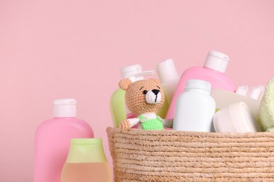 Photo of Baby cosmetic products and toy in wicker basket on pink background, closeup