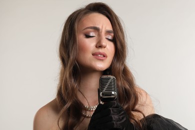 Photo of Beautiful young woman with microphone singing on light grey background