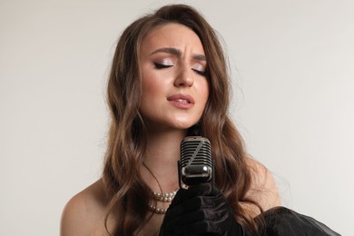 Beautiful young woman with microphone singing on light grey background