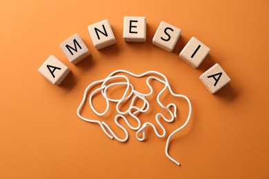 Photo of Word Amnesia and brain made of wires on orange background, flat lay