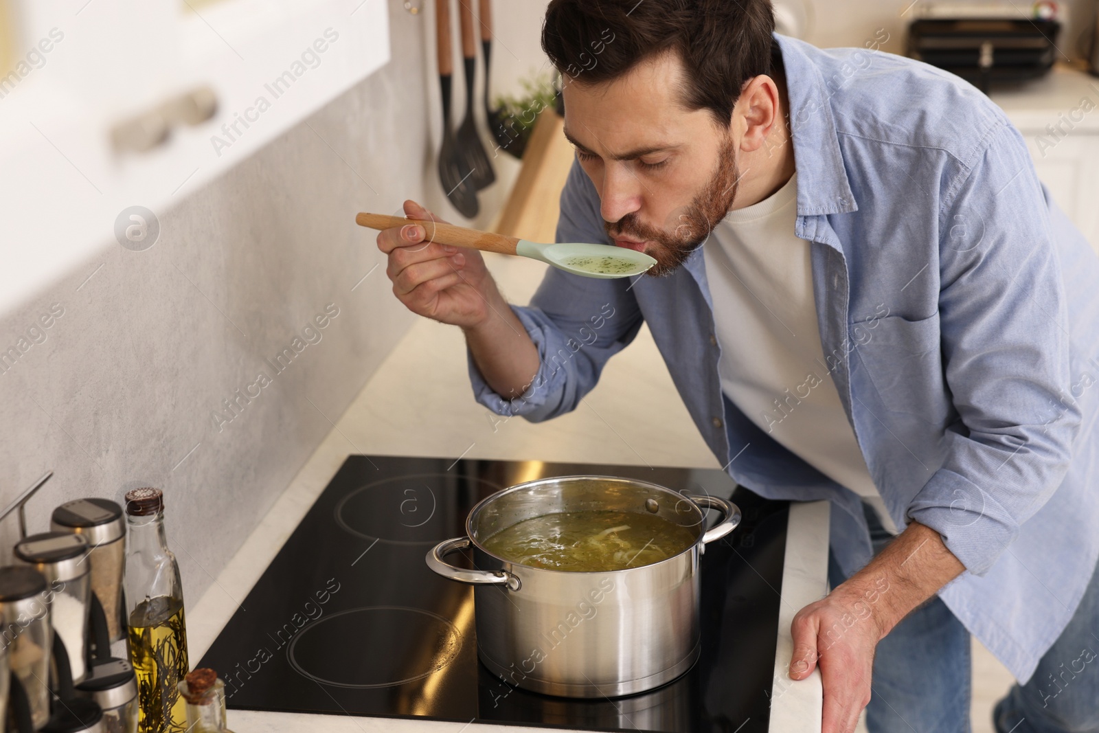 Photo of Man tasting delicious chicken soup in kitchen