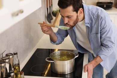 Photo of Man tasting delicious chicken soup in kitchen