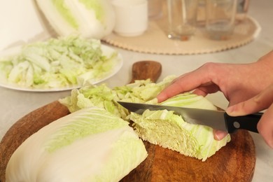 Woman cutting fresh chinese cabbage at kitchen table, closeup