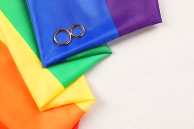 Photo of Rainbow LGBT flag and wedding rings on white background, top view. Space for text