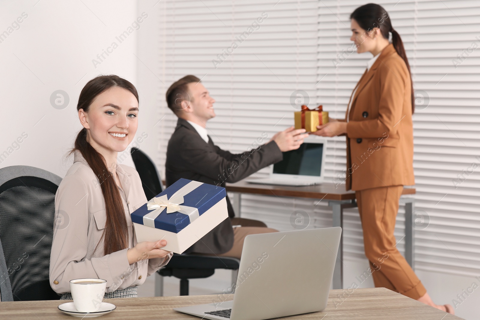 Photo of Happy woman holding gift box and man taking present from his colleague in office