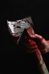 Man holding bloody axe on black background, closeup