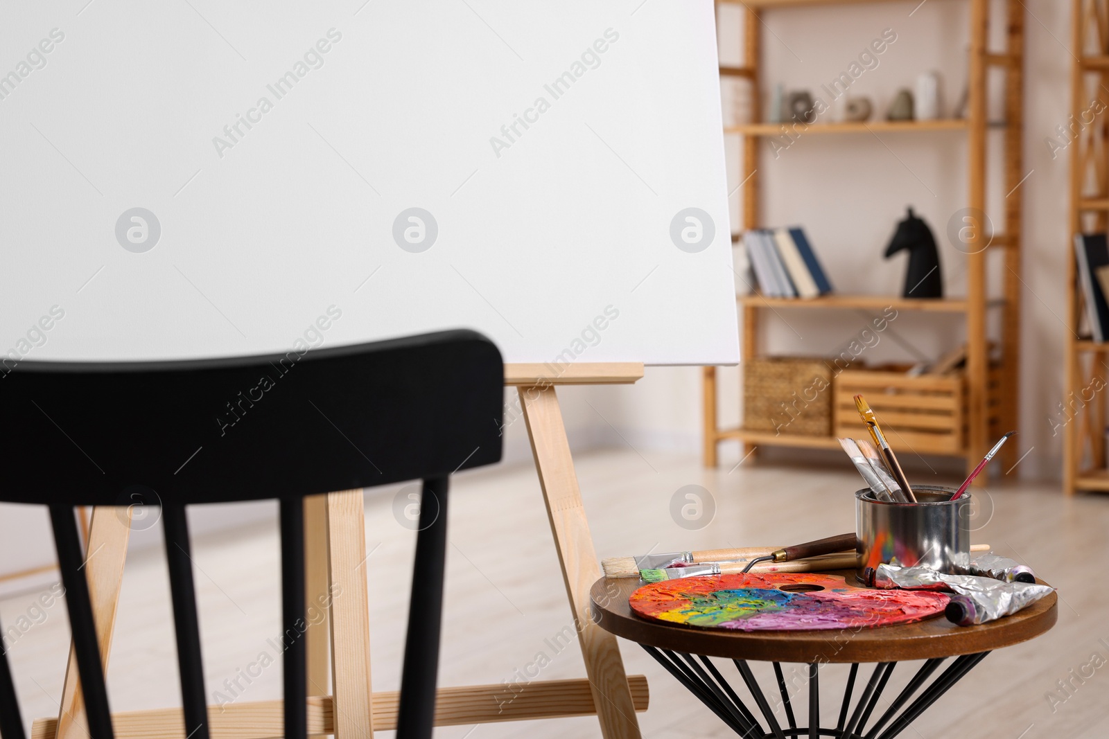 Photo of Wooden easel with blank canvas and different art supplies in studio, closeup