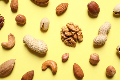 Photo of Different delicious nuts on yellow background, flat lay