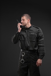 Male security guard using portable radio transmitter on dark background