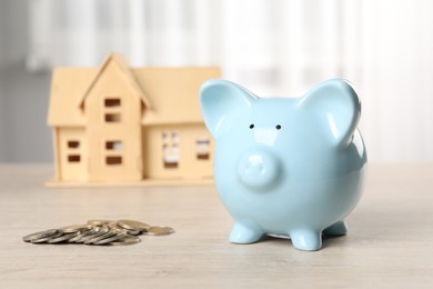 Photo of House model, piggy bank and coins on wooden table indoors, selective focus