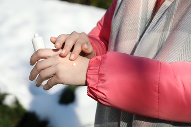 Woman applying moisturizing cream on hands in winter, closeup