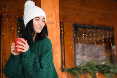 Photo of Pretty woman wearing sweater with cup near wooden terrace in winter