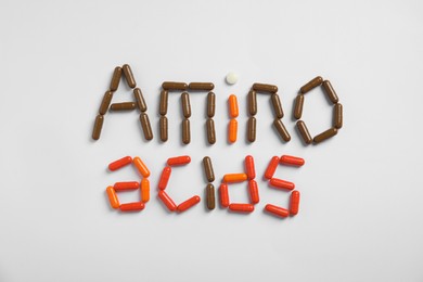 Words "AMINO ACIDS" made with pills on white background, flat lay