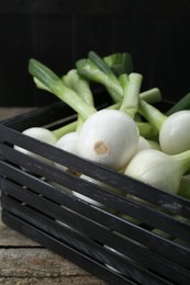 Black crate with green spring onions on wooden table, closeup