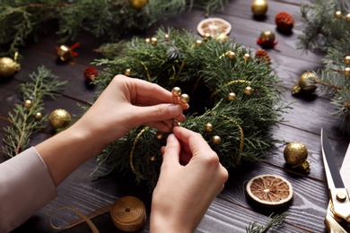 Florist making beautiful Christmas wreath at black wooden table, closeup