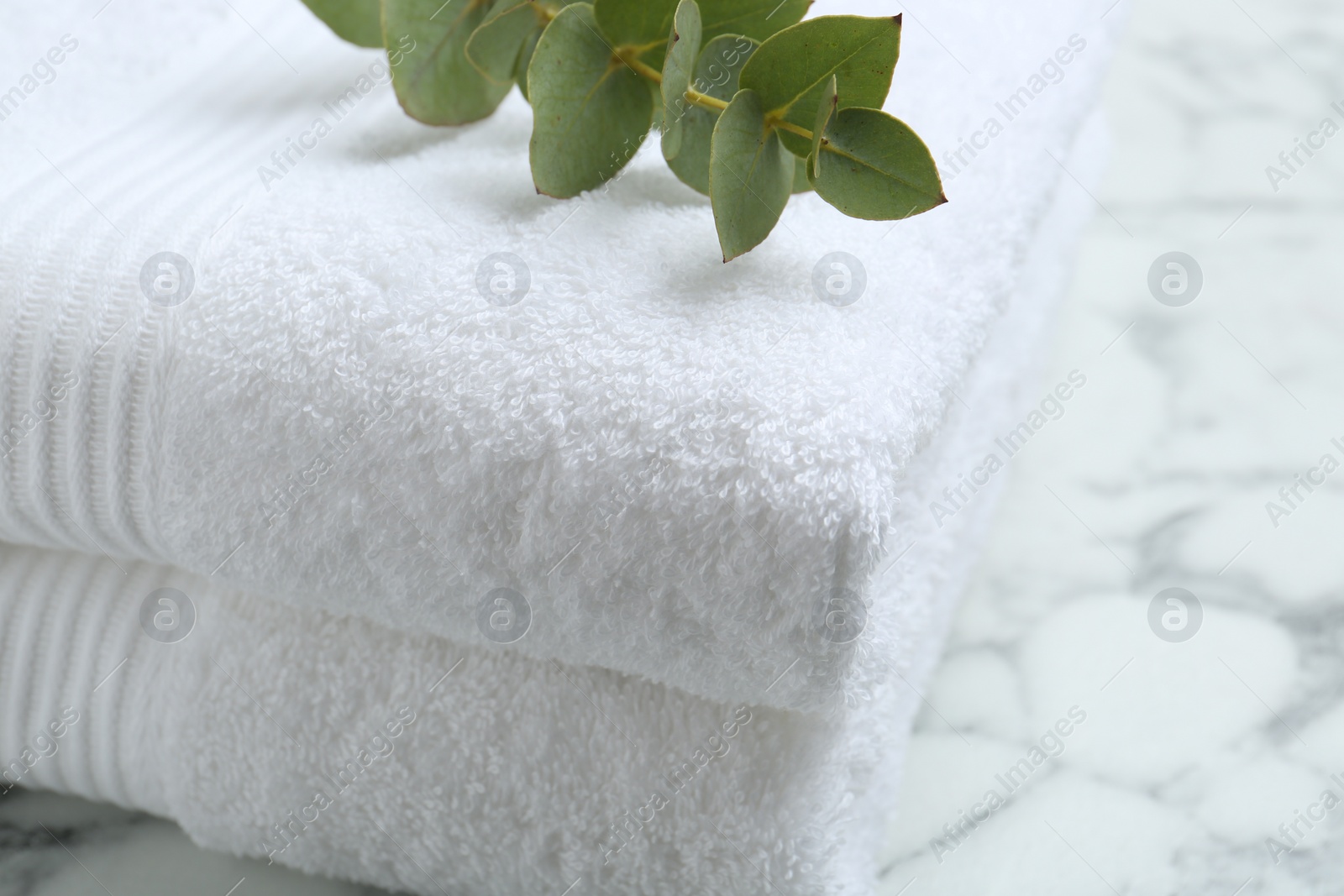 Photo of Folded terry towels and eucalyptus branch on white marble table, closeup