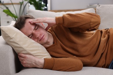 Sad man suffering from headache on sofa indoors