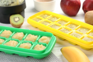 Photo of Banana and kiwi purees in ice cube tray with different fresh fruits white wooden table