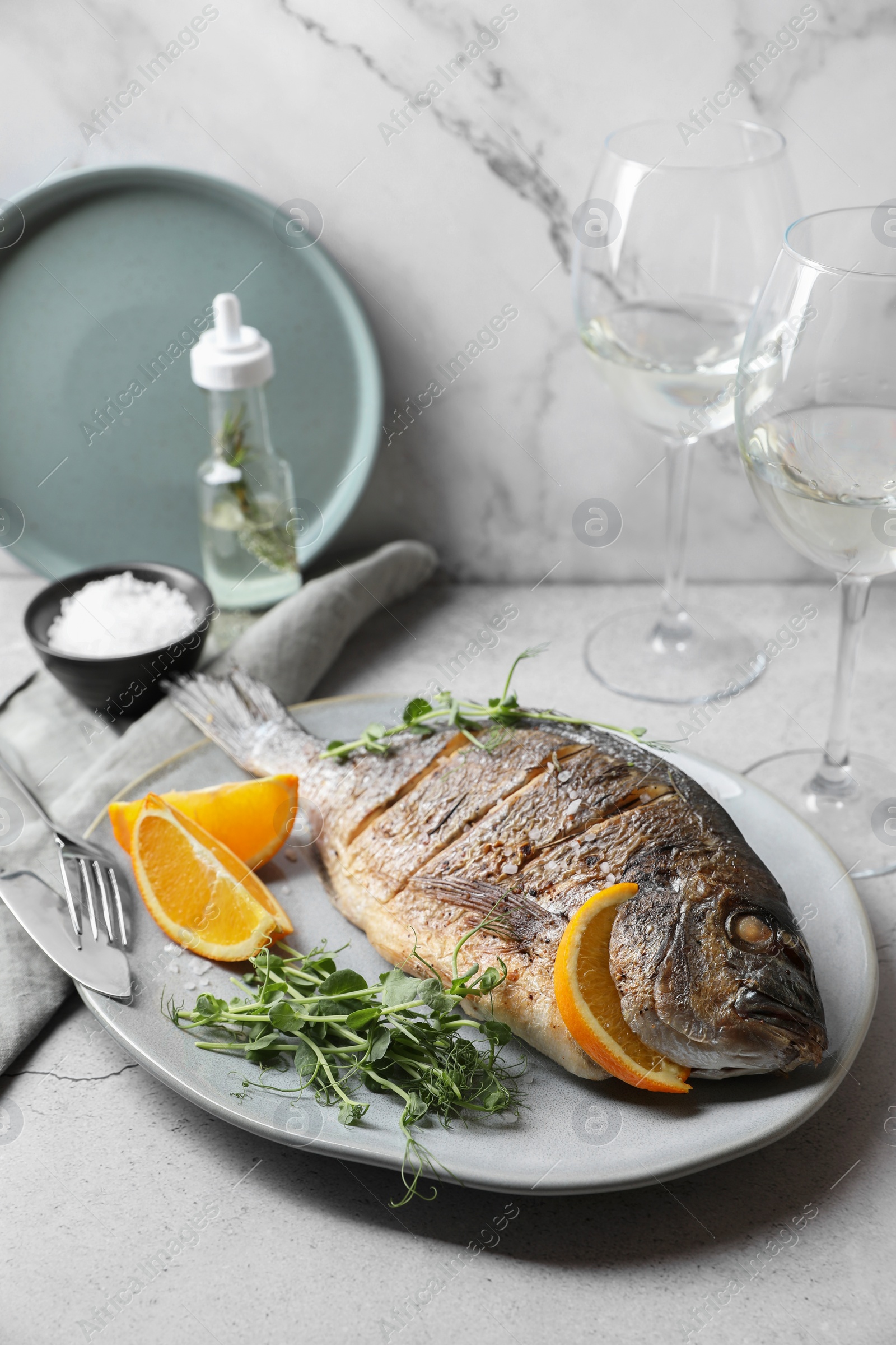 Photo of Seafood. Delicious baked fish served with orange and microgreens on light table