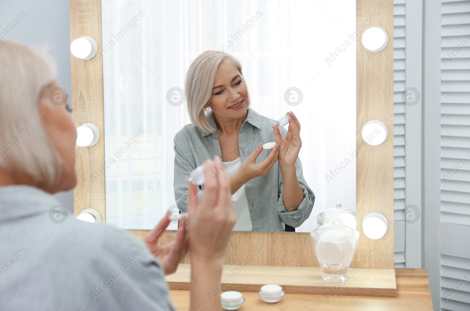 Photo of Portrait of charming mature woman with healthy beautiful face skin and natural makeup applying cream indoors