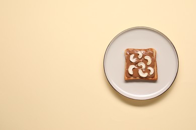 Toast with tasty nut butter and cashews on beige background, top view. Space for text