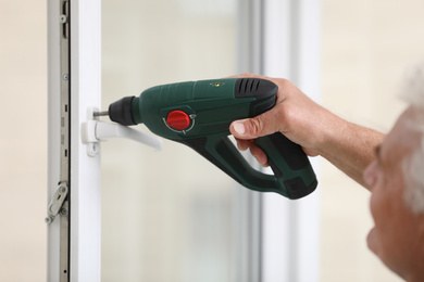 Photo of Construction worker repairing plastic window with electric screwdriver indoors, closeup