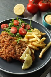 Photo of Tasty schnitzels served with potato fries, tomatoes and arugula on grey table, closeup