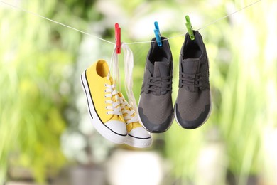 Photo of Different stylish sneakers drying on washing line against blurred background