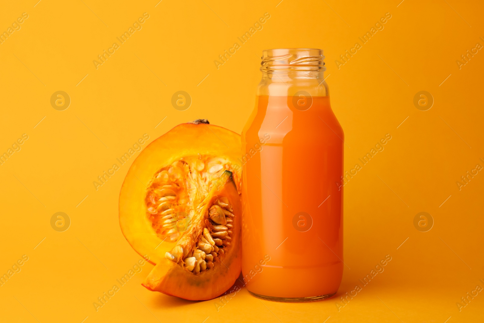 Photo of Tasty pumpkin juice in glass bottle and cut pumpkin on orange background