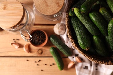 Photo of Fresh cucumbers and other ingredients near jars prepared for canning on wooden table, flat lay