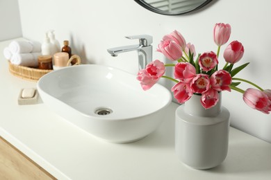 Photo of Vase with beautiful pink tulips and toiletries near sink in bathroom