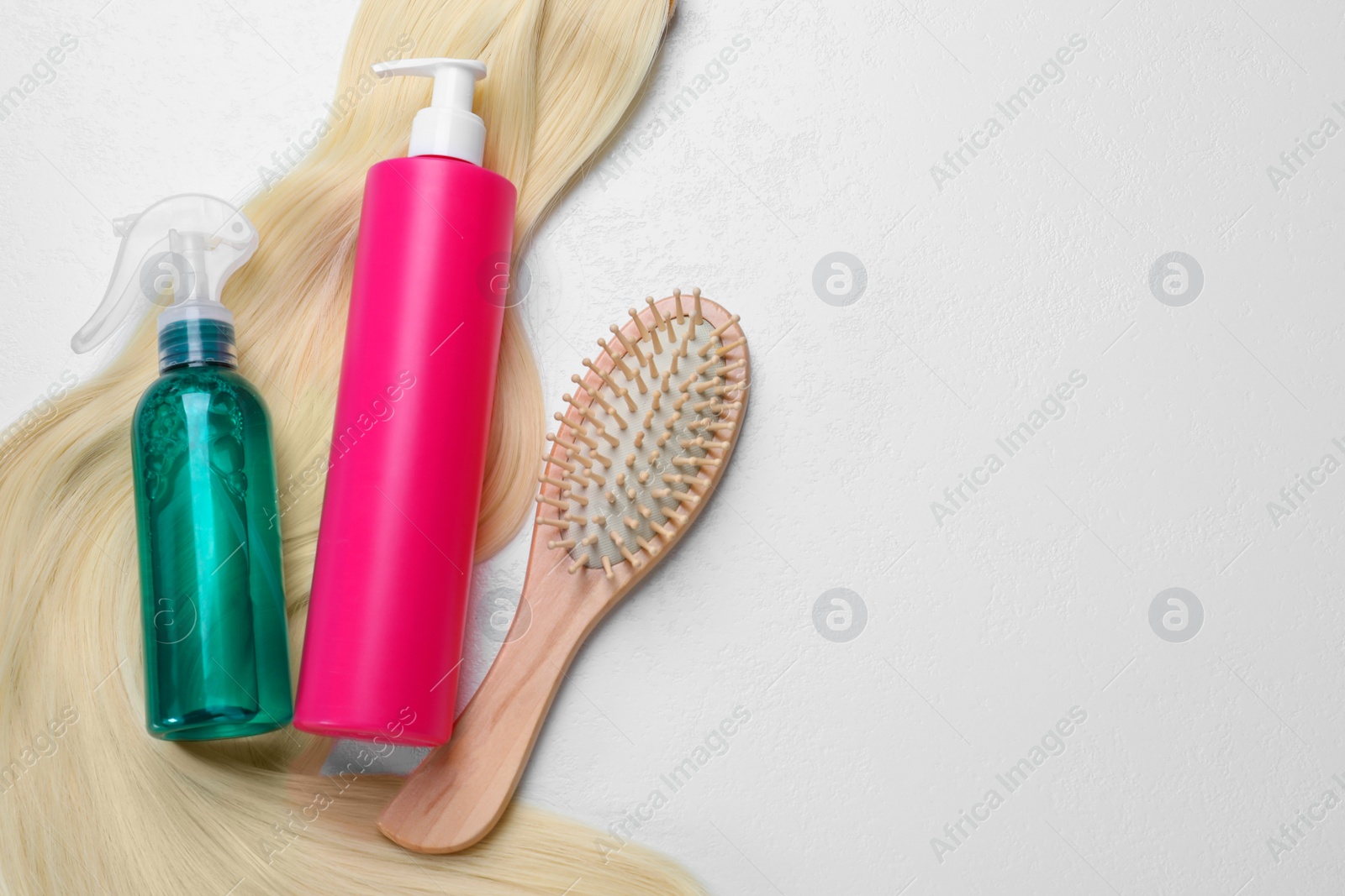 Photo of Spray bottles with thermal protection, lock of blonde hair and hairbrush on white background, flat lay. Space for text