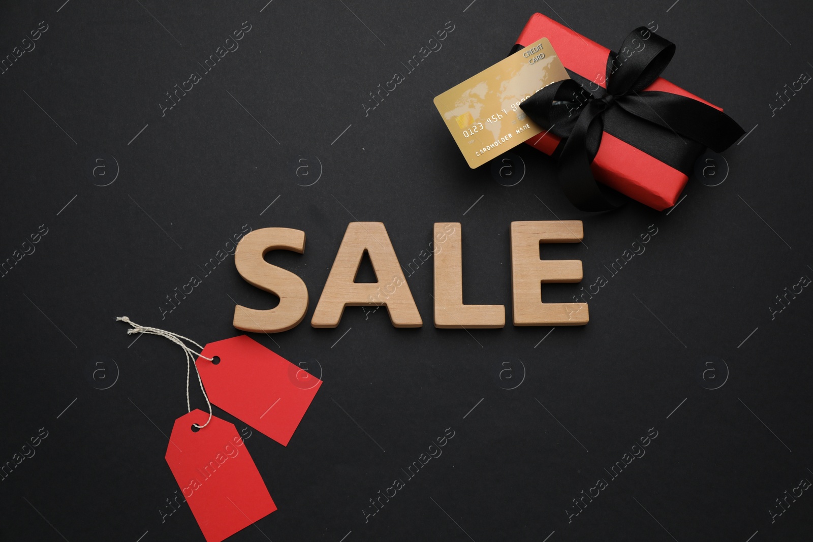 Photo of Word Sale made of wooden letters, price tags, gift box and credit card on black background, flat lay