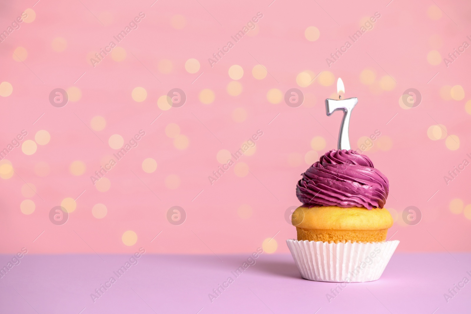 Photo of Birthday cupcake with number seven candle on table against festive lights, space for text