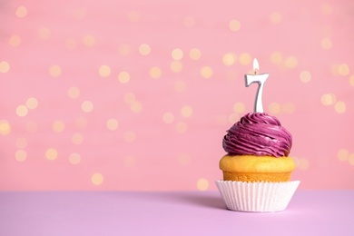 Photo of Birthday cupcake with number seven candle on table against festive lights, space for text