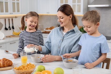 Photo of Mother and her little children having breakfast at table in kitchen