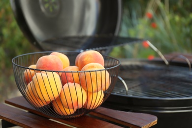 Photo of Fresh peaches on wooden table near modern grill outdoors