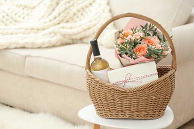 Wicker basket with gifts on table indoors. Space for text