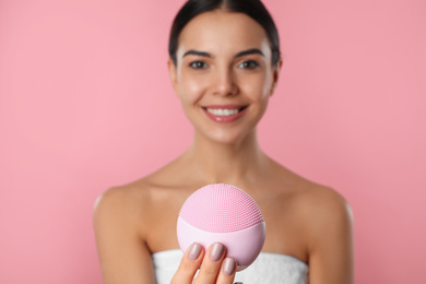 Young woman holding facial cleansing brush on pink background. Washing accessory