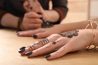 Professional mehndi master making henna tattoo at table, closeup