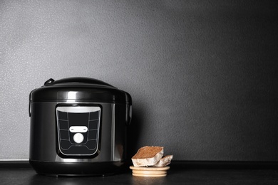 Modern multi cooker and sliced bread on table near dark wall, space for text